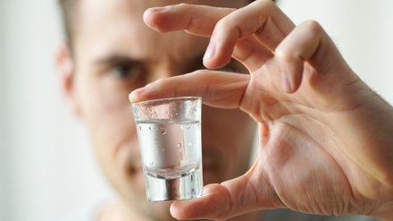 Мужчина держит в руке рюмку водки